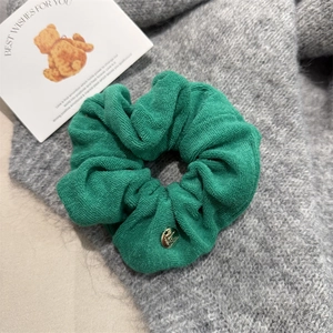 Detailed texture of dark green knitted scrunchie with elegant golden metal tag
