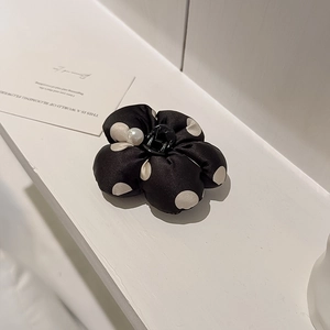 Détail d'une pince à cheveux fleur à pois en satin avec une perle centrale chic