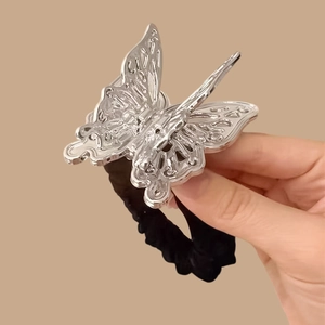 Élastique à cheveux papillon creux argenté avec bande en tissu plissé noir sur fond brun
