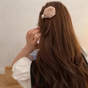 Elegant dried rose fabric hair clip with pearl accent on model's brown wavy hair