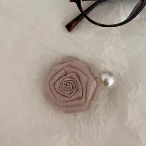 Close-up of pink fabric rose hair clip with pearl detail on white textured paper