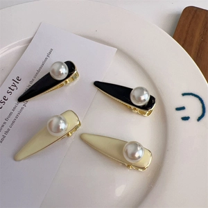 Détail des barrettes à perles noires et blanc crème avec une base élégante en métal doré