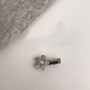 Détail d'une barrette fleur argentée avec perle centrale sur un tissu en maille douce