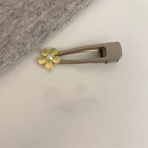 Détail d'une pince à cheveux en métal doré avec une fleur à cinq pétales et une perle