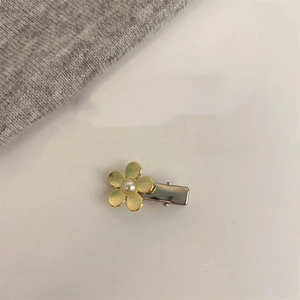 Détail de la pince à cheveux fleur dorée ornée d'une perle blanche sur fond neutre