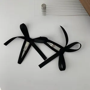 Dettaglio di due eleganti fermagli per capelli con fiocco in raso nero su sfondo
