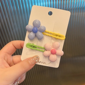 Close-up of set of 2 floral resin hair clips in purple and pink on a white card