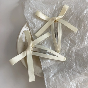 Coppia di eleganti fermagli per capelli in raso crema con fiocco su piatto ceramica