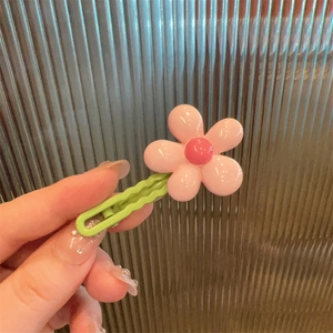 Close-up of pink flower hair clip with a green wavy base held against textured glass