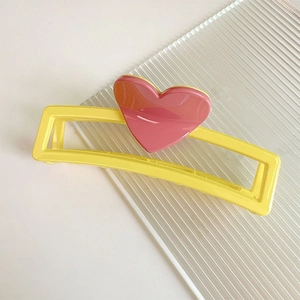 Détail d'une pince à cheveux jaune rectangulaire avec un cœur rose sur une surface en verre