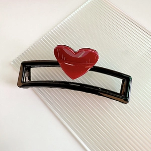 Détail d'une grande pince à cheveux noire 13cm avec cœur rouge sur un fond minimaliste