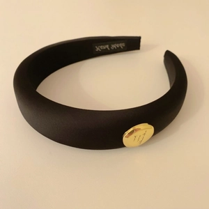 Vue détaillée d'un serre-tête noir en satin rembourré avec bouton doré et étiquette fait main
