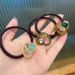 Close-up of three elastic hair ties with colorful rhinestone heart charms on glass background
