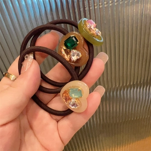 Detail of three heart-shaped resin hair ties featuring colorful embedded rhinestones