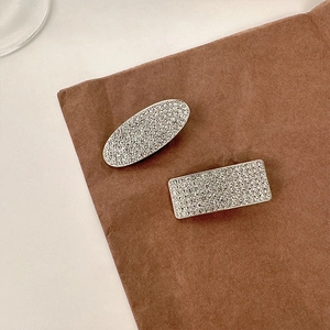 Detailed macro view of silver-tone hair clips featuring pavé-set rhinestones on brown paper