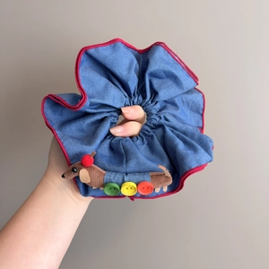 Détail d'un chouchou en jean avec liseré rouge et décoration de petit chien en peluche