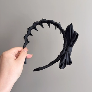 Black fabric headband with rhinestone bow and punk style spikes on a gray background