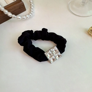 Detailed close-up of a black satin scrunchie with a shimmering square rhinestone embellishment