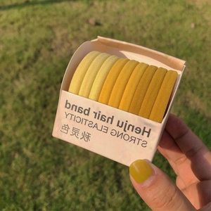 Detail of multi-tone yellow elastic hair bands in box held over a sunny lawn