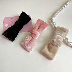 Gros plan de barrettes à nœuds en velours noir, rose et champagne sur fond blanc