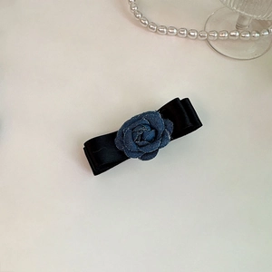 Detail of vintage denim rose and black satin bow hair clip on an elegant beige surface