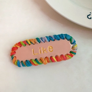 Détail d'une pince à cheveux tricotée colorée avec texte Like et base rose