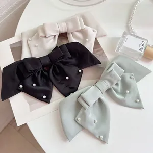 Detail of satin bow hair clips with pearls in beige, black, and green on a white desk