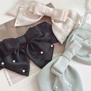 Detailed close-up of satin bow hair clips with pearls in black, white and green