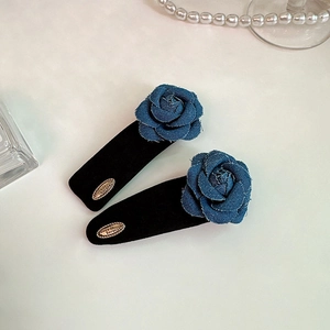 Close-up of vintage denim rose hair clips with velvet base and gold metal engraved tag