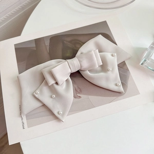 Detail of elegant ivory satin bow hair clip with decorative pearls and silky texture