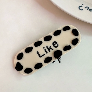 Détail d'une pince à cheveux en acétate crème avec pois noirs et inscription Like