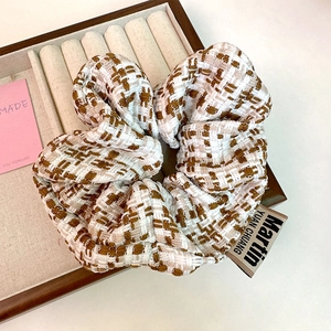 Detailed close-up of a tweed checkered scrunchie on a beige fabric jewelry tray