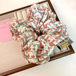 Detailed shot of tweed hair scrunchie with woven label and orange-blue knit texture