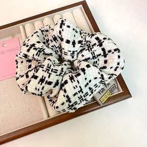 Detailed close-up of a black and white tweed scrunchie with brand label in a velvet box