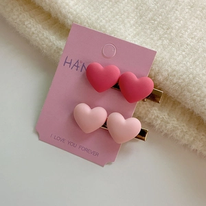 Détail de deux barrettes à cheveux en forme de cœur rose mat sur une carte déco