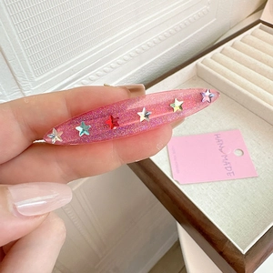 Close-up of pink resin hair clip with colorful star studs and glitter finish detail