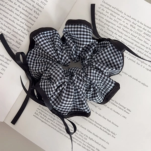 Checkered scrunchie with black ribbon bow on open book, preppy style hair accessory