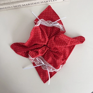 Red polka dot scrunchie with white lace trim and ribbons on a minimalist background