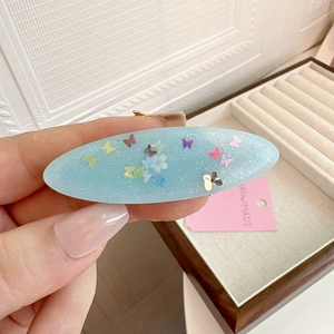 Sparkly light blue oval hair clip with butterfly pattern and handmade label tag