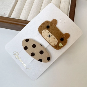 Détail de pince à cheveux ours en feutre et accessoire à pois sur carte de support