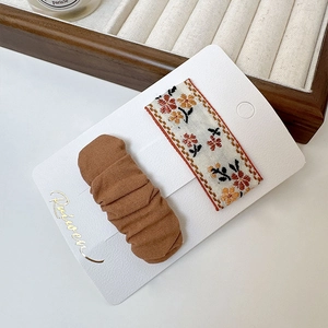 Détail de broderies florales et de barrettes en tissu plissé marron sur carte support