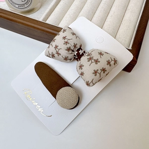 Détail de la pince à cheveux avec nœud floral et clip marron mat sur carte blanche