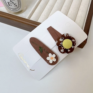 Détail de barrettes en tissu floral avec broderie marguerite sur un plateau de luxe