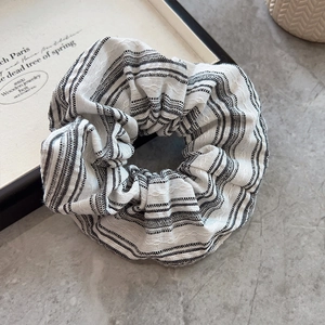 Classic black and white striped fabric scrunchie with pleated texture on stone surface