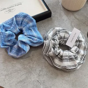 Detail of sea salt blue and striped scrunchie set on a minimalist stone surface