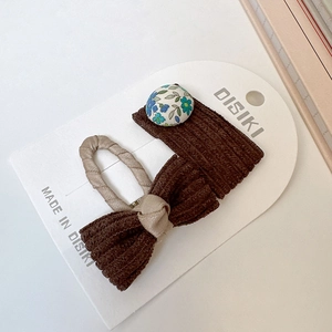 Vue macro de barrettes en velours côtelé marron avec détail floral sur carte blanche