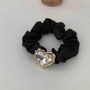 Dettaglio di un elastico scrunchie in raso nero con un grande cuore di cristallo lucido