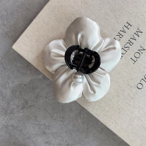 Detail of cream satin flower hair claw with pearl accent on elegant book backdrop