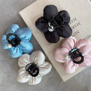 Detailed view of satin flower hair claws in four colors with pearl center on book