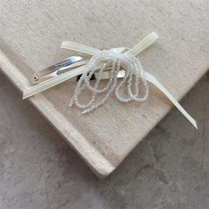 Elegant beaded bow hair clip with tassel pearls on minimalist fabric background